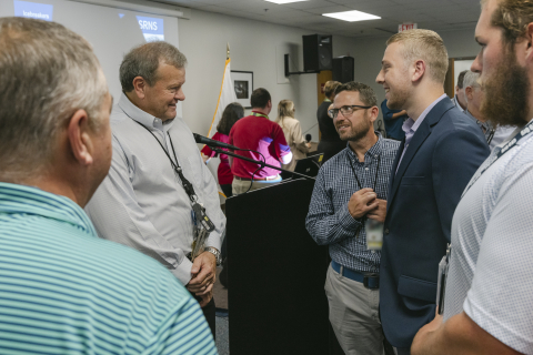 A group of four college interns stand beside an older man and speak to hi