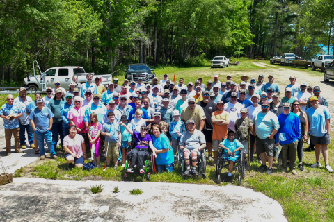 A large group of people stand and sit outside while posing for a group picture