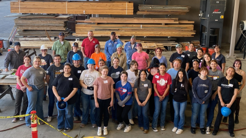 A large group photo of young girls inside a laboratory with lots of wooden beams behind them