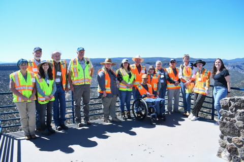 A group of people stand outside at an overlook area in New Mexico, they wear orange and yellow safety vests