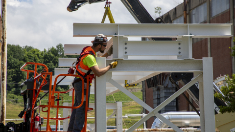 A man in a construction outfit works on building a white metal bridge