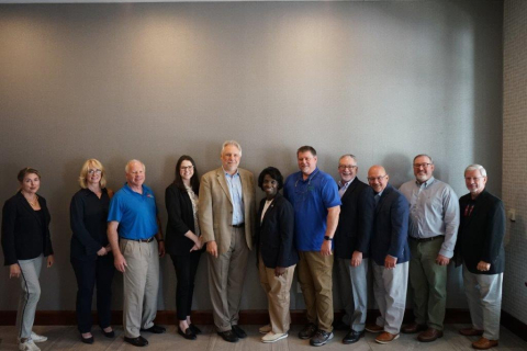 A group of professionals pose for a group picture in front of a dark gray wall