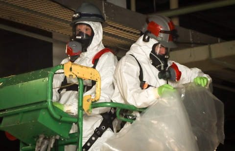 Workers use an aerial lift to remove asbestos pipe insulation.