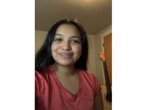 Reyna Morales Lumagui wearing a red shirt with an acoustic guitar in the background.