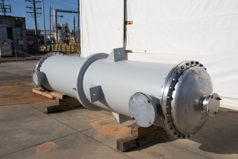 A long metal condenser tank on top of a stand outside of a facility building