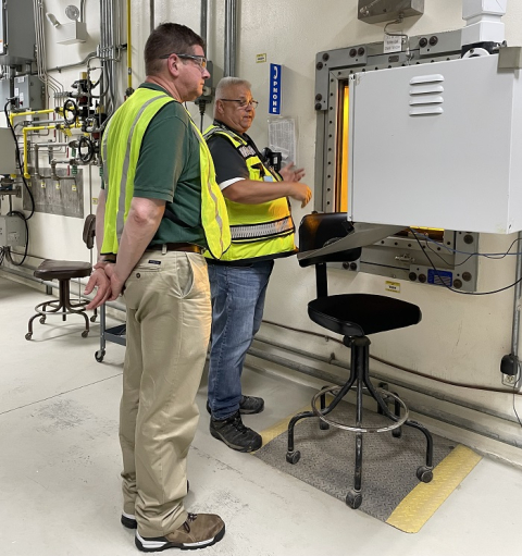 Two men stand inside a facility building and look at a large white machine