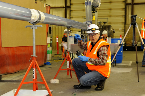 A worker in protective gear crouched beneath a pipe