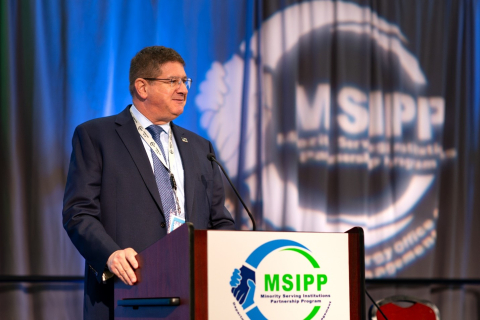 An EM leader stands on a stage behind a podium 
