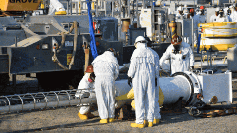 A rotation of images of a large metal and white machine on the ground with workers standing around it 