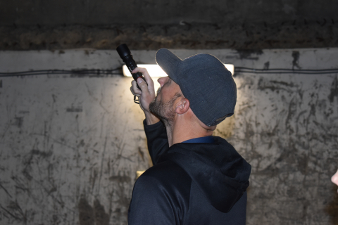 A man stands in a dark room and holds a flashlight upwards