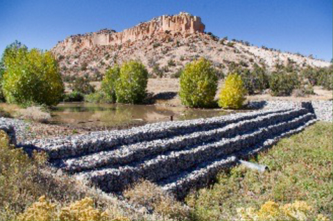 A stair-step shaped structure made from stones outside beside a small body of water and grass