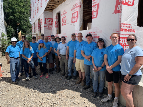 A group of people in blue t-shirts stand beside a house that is in the process of being built
