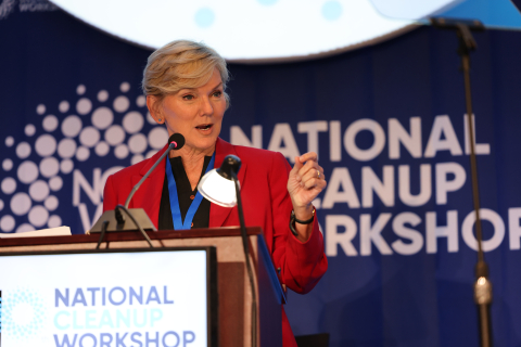 A woman standing on a stage speaking at a podium while looking out into the audience