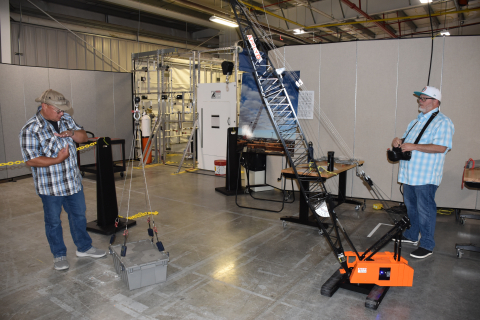 Two employees work on and take photographs of an orange machine with a ladder coming out from it