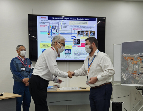 Two men stand in a room wearing masks and shake hands