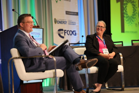 A DOE leader sits on stage beside a man moderating the session, they speak to the audience