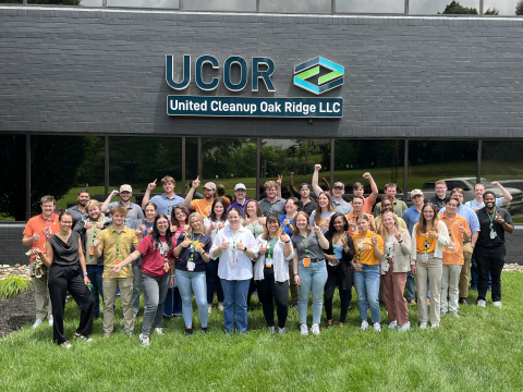 A large group of people pose for a photo outside a gray building 