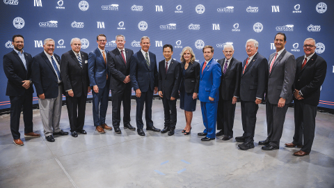 A group of people in suits stand in front of a dark blue backdrop and pose for a group picture