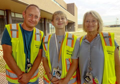 Two parents pose for a picture with their son, they all are wearing yellow safety vests