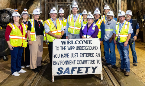 A group of people in white safety hats and yellow safety vests pose for a group picture in an underground storage facility