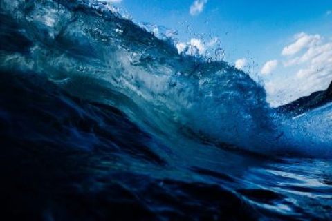 Picture of a wave crashing with blue sky in the background