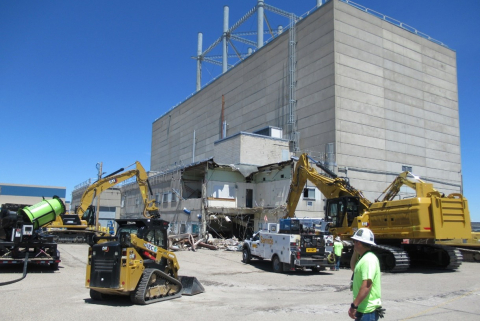 A large, concrete building with yellow construction vehicles and workers outside of it