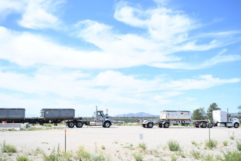 An open valley with blue skies and fluffy white clouds and two large trucks carrying materials
