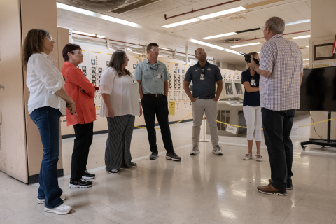 A man stands with his back to the camera and gives a tour to a group of six people