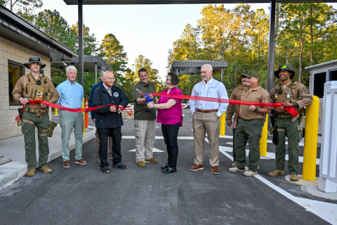A group of people stand in a row and cut a red ribbon