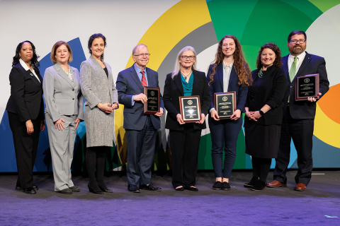 A group of individuals standing together holding plaques at an awards ceremony.