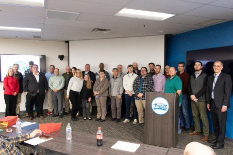 A group of people in a conference room stand and pose for a picture