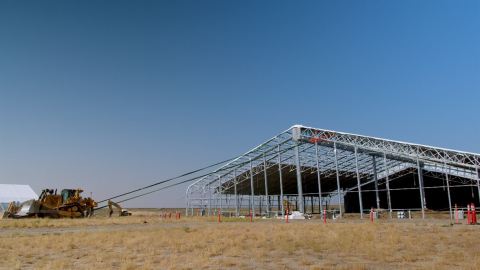 A photo a building only made out of beams, it its attached on ropes to a demolition vehicle