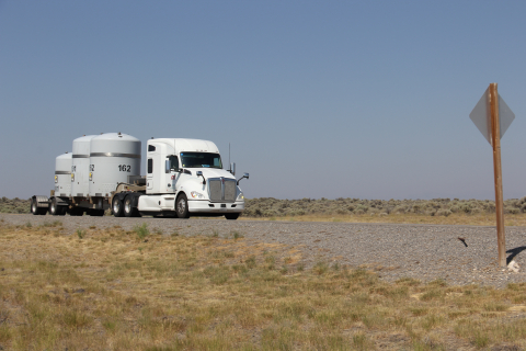 A white eighteen-wheeler truck drives on a road with white tanks on the back