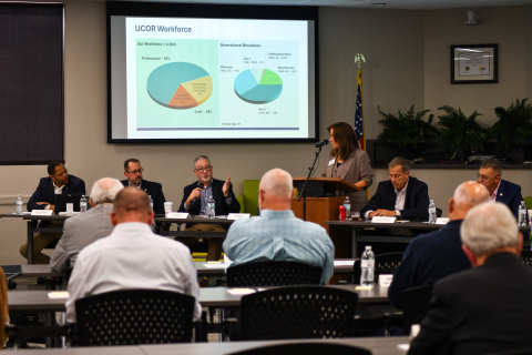 A panel of professionals sitting at the front of a room with a powerpoint presentation behind them, they address the crowd