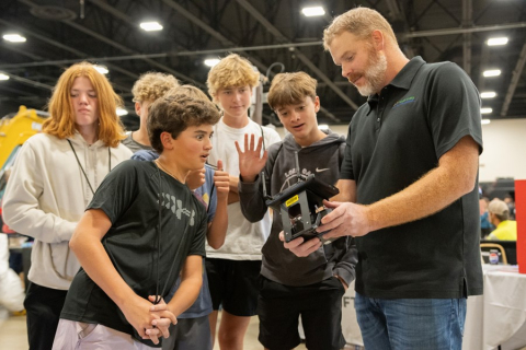 A group of students stand around an iPad held by a professional and they look at the screen