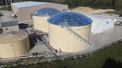 Aerial view of three large tan tanks, surrounded by facility buildings