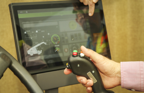 An upclose shot of a Caucasian hand using a control lever with a monitor in the background