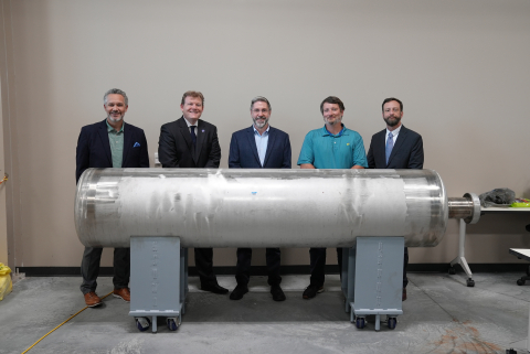 Five people stand and pose for a picture behind a large metal canister on display