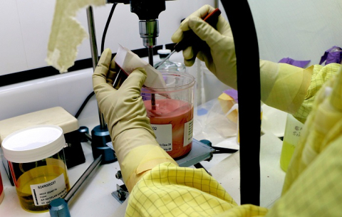 An upclose shot of a scientist wearing gloves and protective gear while preparing a red slurry in a beaker