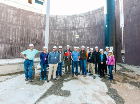 A group of people in white safety hats smile for a group photo