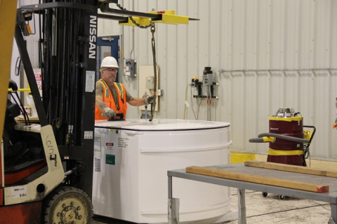 A man in protective gear works on a small white tank with a black machine on  it