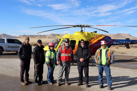A group of six people stand outside in front of a helicopter