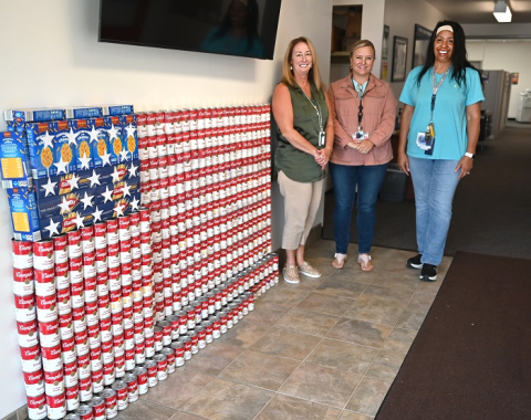 Canned and boxed food stacked to create an American flag with three woman posing for a picture beside it