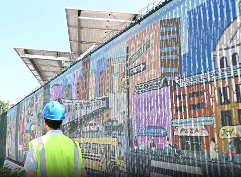 Person in a blue hardhat and safety vest walking past a colorful mural