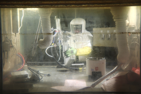 An employee in a white hazmat suits work with materials inside a hot cell