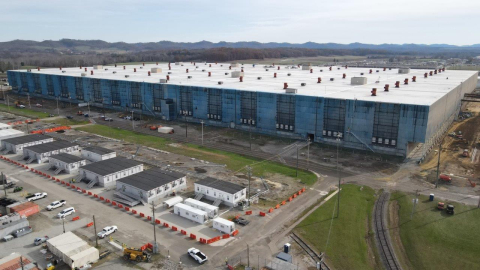 An aerial view of a large facility building with smaller buildings and cars around it