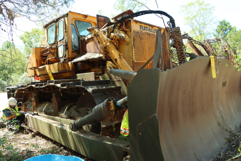 a large yellow work vehicle in the woods with employees standing around it