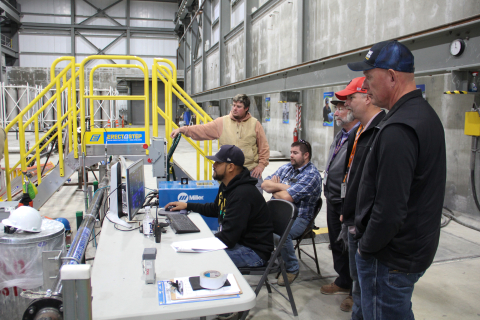 A group of employees inside a building looking at a computer that one man is working at