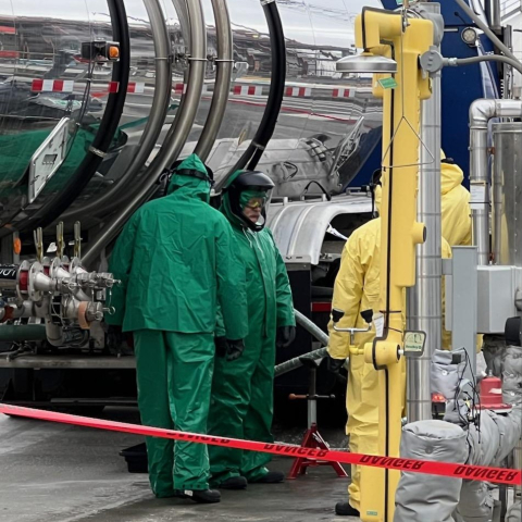 Employees in hazmat gear stand beside a large truck