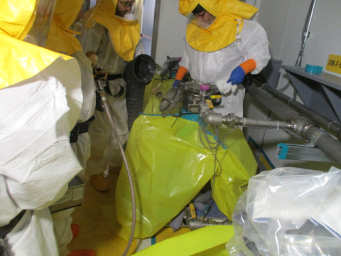Three employees in hazmat suits removing hazardous equipment